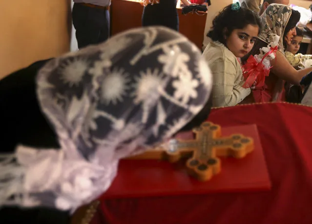 An Assyrian Christian girl, background, holds a candle as she looks at a woman kissing the cross during Mass marking the traditional Palm Sunday procession at the Assyrian church in east of Beirut, Lebanon, Sunday, March 29, 2015. Streams of Christians gathered Sunday to celebrate the path of Jesus Christ's last journey into Jerusalem, when his followers laid palm branches in his path, before his crucifixion. (Photo by Hussein Malla/AP Photo)