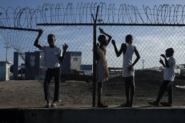 Youths stand at a gate along the seashore in the La Saline neighborhood of Port-au-Prince, Haiti, Monday, July 19, 2021. The country of more than 11 million people are still reeling from the July 7 killing of President Jovenel Moise. (Photo by Matias Delacroix/AP Photo)