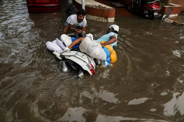 A man helps to lift a scooter of a man, as he fell at a waterlogged street after heavy rains in New Delhi, India, September 1, 2021. (Photo by Anushree Fadnavis/Reuters)