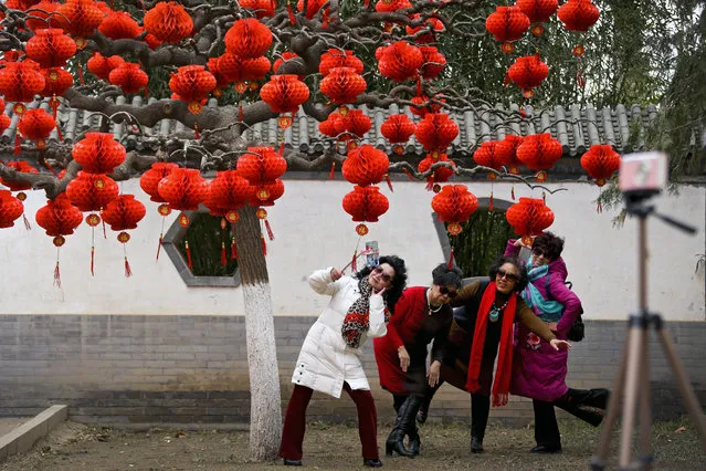 In this Wednesday, January 30, 2019, photo, women take a selfie near a tree decorated with red lanterns ahead of the Lunar New Year at Ditan Park in Beijing. (Photo by Andy Wong/AP Photo)