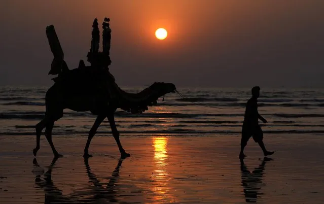 A Pakistani man and his camel are silhouetted, against the last sunset of 2023 at Clifton beach in Karachi, Pakistan, Sunday, December 31, 2023. (Photo by Fareed Khan/AP Photo)