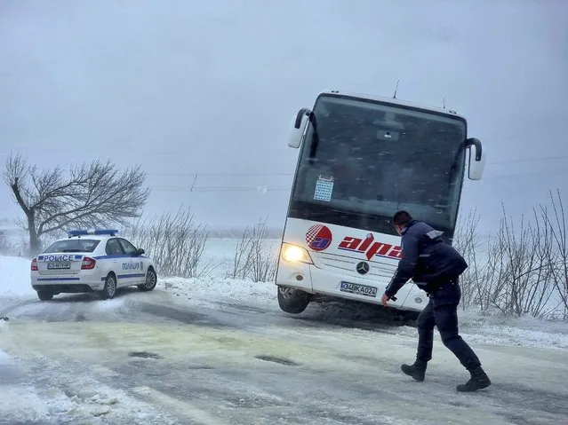 Policeman walks in front of a bus gone of the road near town of Dobrich, Bulgaria, Sunday, November 19 2023. Gale-force winds and heavy rain and snow hit large parts of Bulgaria claiming the lives of two people and causing severe damages and disrupting power supply in towns and villages, officials said on Sunday. (Photo by Bulgarian News Agency via AP Photo)