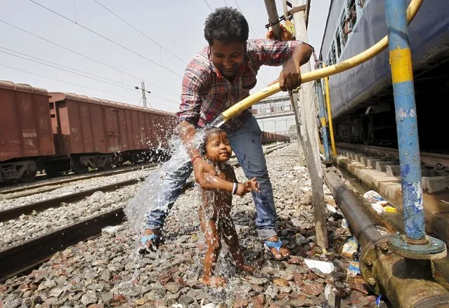 A passenger bathes an child using a pipe that supplies water to trains at a railway station on a hot summer day in the northern Indian city of Allahabad April 23, 2015. Temperatures in Allahabad on Thursday reached to 42 degree Celsius (107.6 degree Fahrenheit), according to India's metrological department website. (Photo by Jitendra Prakash/Reuters)