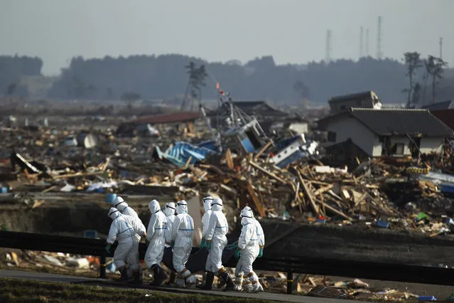 In this April 15, 2011 file photo, Japanese police officers in protective suits carry a victim at a tsunami-devastated area in the town of Namie as towers of the crippled Fukushima Dai-ichi nuclear power plant are seen in the distance, top right, in Fukushima Prefecture, northeastern Japan. “One month after the disaster struck, we slipped into the evacuation zone around the Fukushima Dai-ichi nuclear facility. (Photo by Hiro Komae/AP Photo)