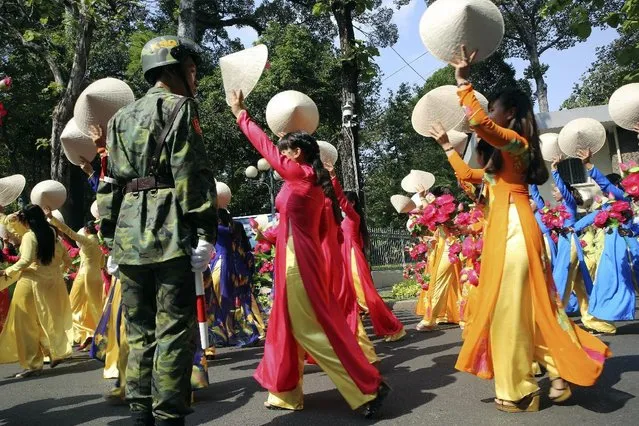 A Vietnamese soldier stands guard as a group of women wave their conical hats during a parade celebrating the 40th anniversary of the end of the Vietnam War which is also remembered as the fall of Saigon, in Ho Chi Minh City, Vietnam, Thursday, April 30, 2015. (Photo by Na Son Nguyen/AP Photo)