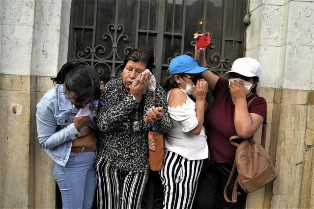 Women take cover from tear gas thrown by police during clashes with anti-government protesters in Lima, Peru, Thursday, January 19, 2023. Protesters are seeking immediate elections, the resignation of President Dina Boluarte, the release from prison of ousted President Pedro Castillo and justice for protesters killed in clashes with police. (Photo by Martin Mejia/AP Photo)