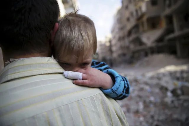 A man holds a child that he said survived shelling from forces loyal to President Bashar al-Assad, along a street in Duma neighborhood in Damascus, November 17, 2013. (Photo by Bassam Khabieh/Reuters)