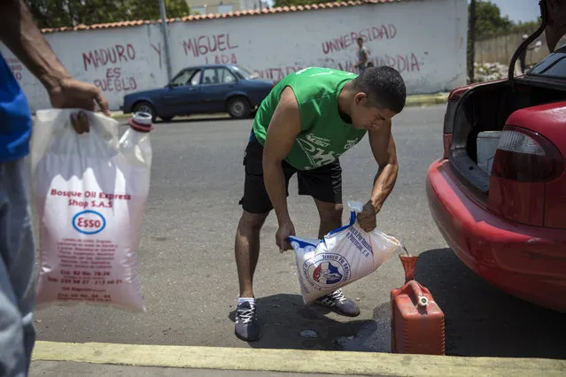 Jesus Gonzales fills a container with bagged gasoline he bought at extra cost at a fuel station, in order to not wait in the longer line in Cabimas, Venezuela, Saturday, May 18, 2019. U.S. sanctions on oil-rich Venezuela appear to be taking hold, resulting in mile-long lines for fuel in the South American nation’s second-largest city, Maracaibo. (Photo by Rodrigo Abd/AP Photo)