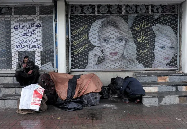 People cover themselves as they sit in front of a beauty salon in Kabul, Afghanistan, January 3, 2022. (Photo by Ali Khara/Reuters)