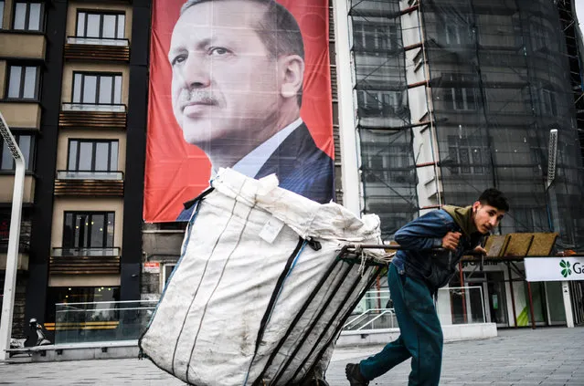 A man pulls a cart in front of a huge portrait of Turkish President Recep Tayyip Erdogan on Taksim Square in Istanbul on March 15, 2017. Turkey will hold its constitutional referendum on April 16, 2017. The controversial changes seek to replace the parliamentary system and move to a presidential system which would give President Recep Tayyip Erdogan executive authority. (Photo by Bulent Kilic/AFP Photo)