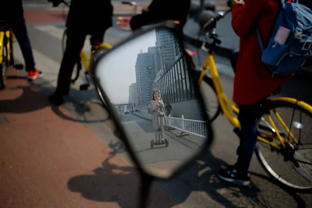 A Chinese woman riding on an electric self-balancing scooter is reflected in a wing mirror on a street in Beijing, China, 29 March 2017. (Photo by Wu Hong/EPA)