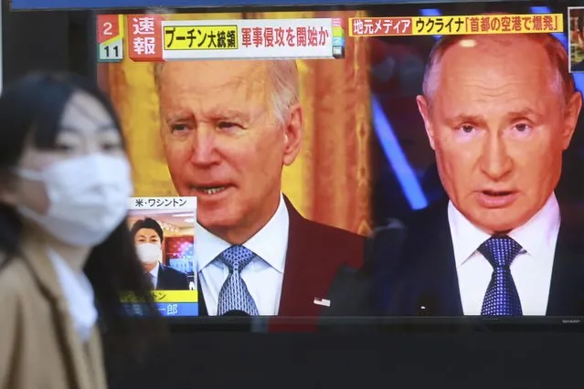A woman walks past a TV screen showing images of Russia's President Vladimir Putin and U.S. President Joe Biden in Tokyo, Thursday, February 24, 2022. Russian troops launched a wide-ranging attack on Ukraine on Thursday, as President Vladimir Putin cast aside international condemnation and sanctions and warned other countries that any attempt to interfere would lead to “consequences you have never seen”. (Photo by Koji Sasahara/AP Photo)