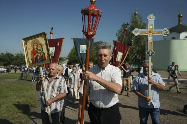 People carry an Orthodox cross and icons walk to attend a memorial service at the crash site of the Malaysia Airlines Flight 17, near the village of Hrabove, eastern Ukraine, Friday, July 17, 2015. (Photo by Mstyslav Chernov/AP Photo)