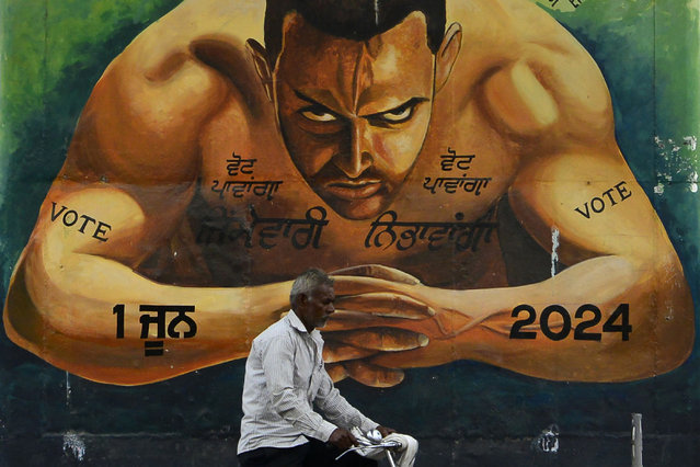 A man rides a bicycle past a mural portraying Bollywood actor Aamir Khan and slogans to encourage people to cast their vote, in Jalandhar on May 10, 2024 ahead of the fourth phase of voting of India's general election. (Photo by Shammi Mehra/AFP Photo)