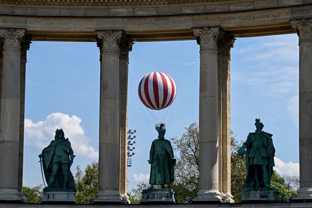 A balloon with 6000 cubic meters of helium, the Hungarian capital's latest tourist attraction, is seen in the air behind statues of Hungarian kings near Heroes' Square in Budapest on May 1, 2022, on the day of its inauguration. (Photo by Attila Kisbenedek/AFP Photo)