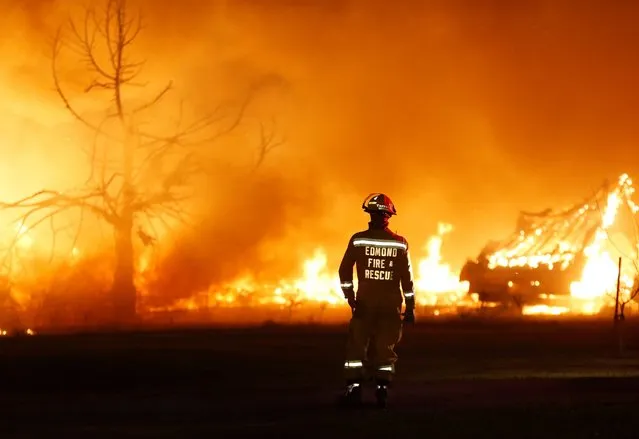 An Edmond firefighter looks on at a fire raging in a mobile home park during wildfires in Logan County, Okla., May 4, 2014. Firefighters worked through the night and into the early morning to battle the large wildfire that destroyed at least six homes, and left at least one person dead, after a controlled burn spread out of control in central Oklahoma. (Photo by Nate Billings/AP Photo/The Oklahoman)