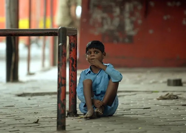 In this photograph taken on May 20, 2014 nine year old Indian boy Lakhan Kale is tied with a cloth rope around his ankle, to a bus-stop pole in Mumbai. (Photo by Punit Paranjpe/AFP Photo)