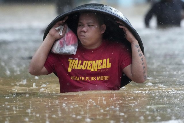 A resident uses a laundry tub to protect him from rain as he wades along a flooded street caused by Tropical Storm Yagi, locally called Enteng, on Monday, September 2, 2024. (Photo by Aaron Favila/AP Photo)