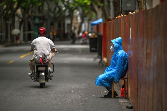 A worker sits next to a fence erected to close a residential area under Covid-19 lockdown in the Huangpu district of Shanghai on June 10, 2022. (Photo by Hector Retamal/AFP Photo)