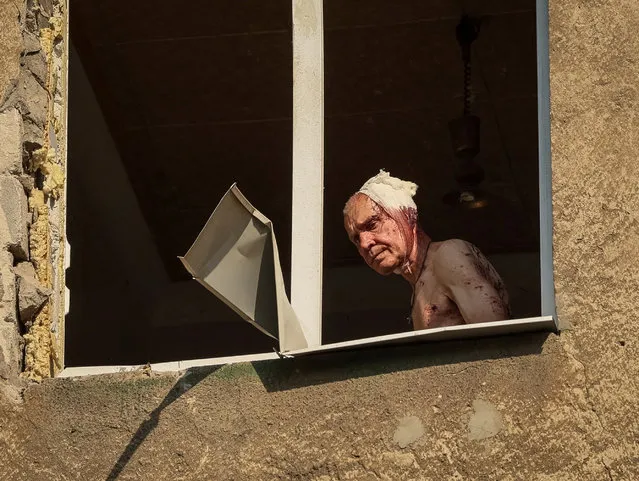 Wounded local resident Volodymir, 66, looks out from inside his flat in an apartment building destroyed in a military strike, amid Russia's invasion, in Kramatorsk, Ukraine July 7, 2022. (Photo by Gleb Garanich/Reuters)