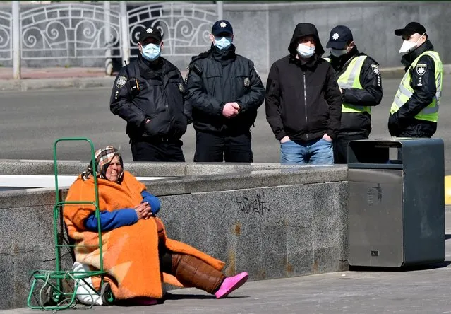 An elderly homeless woman asks for alms as police wearing face masks, amid concerns over the spread of the novel coronavirus COVID-19, patrol the streets of the Ukrainian capital of Kiev on April 5, 2020 a day before the lockdown tightening, imposed by authorities to attempt to prevent the spread of COVID-19 coronavirus disease. (Photo by Sergei Supinsky/AFP Photo)