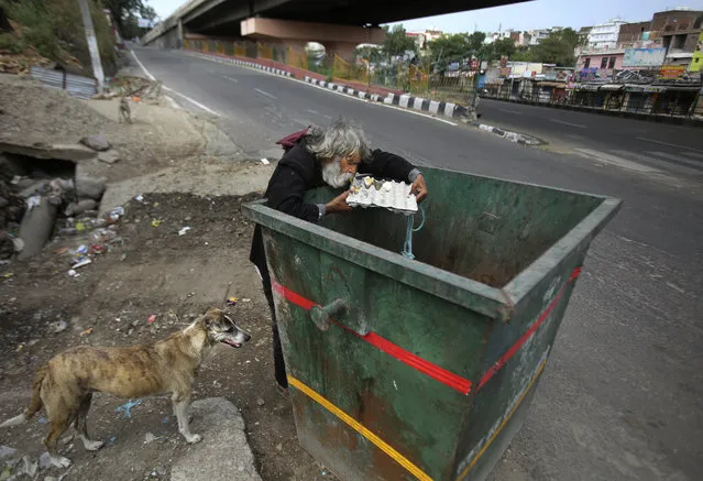 An Indian homeless man eats eggs discarded in a garbage bin during lockdown to curb the spread of new coronavirus on the outskirts of Jammu, India, Sunday, May 10, 2020. India's lockdown entered a sixth week on Sunday, though some restrictions have been eased for self-employed people unable to access government support to return to work. (Photo by Channi Anand/AP Photo)