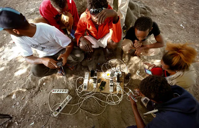 Migrants sit with their mobile phones around power plugs near a temporary WI-FI hotspot in a makeshift camp at a park near the San Giovanni railway station in Como, Italy August 12, 2016. (Photo by Arnd Wiegmann/Reuters)
