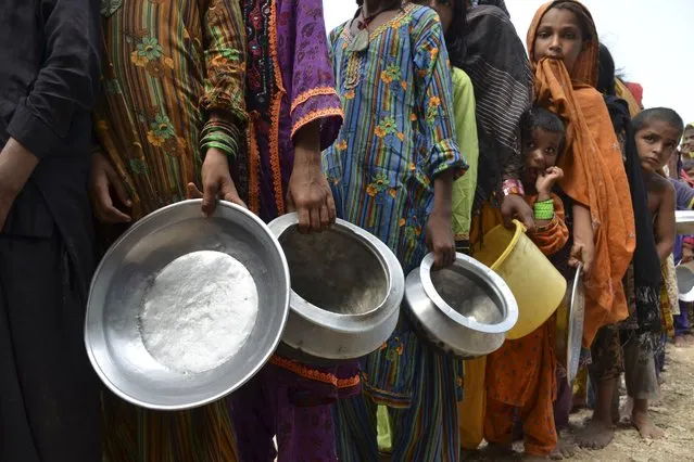 Displaced flood-affected people stand in a queue to receive food being distributed by Saylani Welfare Trust at a makeshift camp in flood-hit Sehwan of Sindh province on September 13, 2022. (Photo by Husnain Ali/AFP Photo)