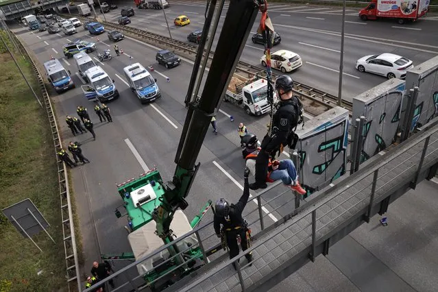 Police rescuers remove an activist from the group “Last Generation” who had glued herself to a structure over the ring highway on October 19, 2022 in Berlin, Germany. Activists climbed onto at least six similar structures around Berlin in an effort to disrupt traffic and bring attention to the urgency of climate change. (Photo by Sean Gallup/Getty Images)