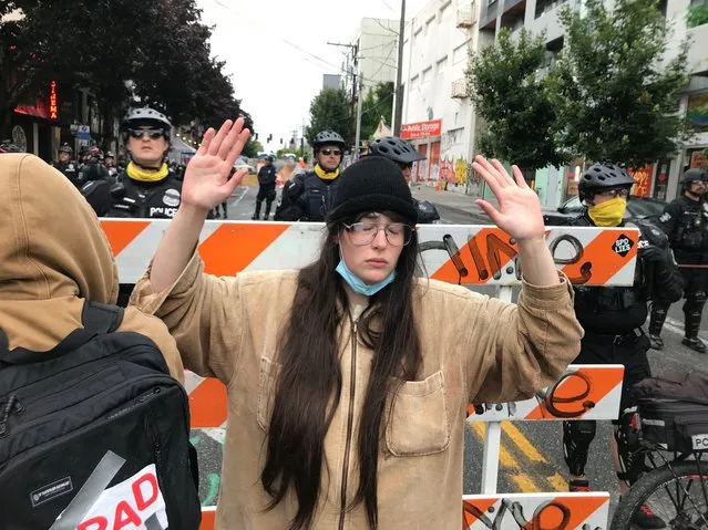 A protester stands with her hand up in front of a road blocked by Seattle police in the Capitol Hill Organized Protest zone early Wednesday, July 1, 2020. Police in Seattle have torn down demonstrators' tents in the city's so-called occupied protest zone after the mayor ordered it cleared. (Photo by Aron Ranen/AP Photo)