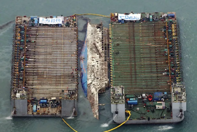 Workers try to raise the sunken Sewol ferry between two barges during a salvage operation in waters off Jindo, South Korea, on March 23, 2017. The 6,800-ton South Korean ferry emerged from the water, nearly three years after it capsized and sank into violent seas off the country's southwestern coast, an emotional moment for the country that continues to search for closure to one of its deadliest disasters. (Photo by Choi Young-su/Yonhap via AP Photo)