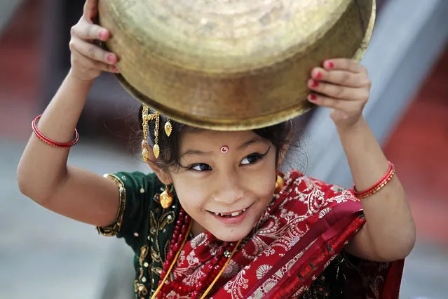 A young Nepalese girl wearing traditional attire plays with a vessel while waiting for the Kumari puja to start at Hanuman Dhoka temple, in Kathmandu, Nepal, Wednesday, September 14, 2016. Girls under the age of nine gathered for the Kumari puja, a tradition of worshiping young prepubescent girls as manifestations of the divine female energy. The ritual holds a strong religious significance in the Newar community that seeks divine blessings to save small girls from diseases and bad luck in the years to come. (Photo by Niranjan Shrestha/AP Photo)