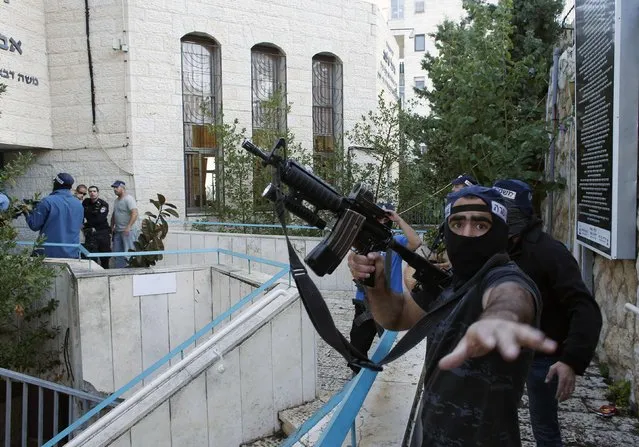 An Israeli police officer gestures as he holds a weapon near the scene of an attack at a Jerusalem synagogue November 18, 2014. Two suspected Palestinian men armed with axes and knives killed four people in a Jerusalem synagogue on Tuesday before being shot dead by police, Israeli police and emergency services said, the deadliest such attack in the city in years. (Photo by Ronen Zvulun/Reuters)