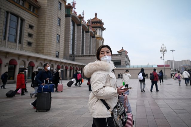 A woman looks back as she makes her way to the entrance of the Beijing railway station in the Chinese capital on January 7, 2023, as annual migration begins with people heading back to their hometowns for Lunar New Year celebrations. (Photo by Wang Zhao/AFP Photo)
