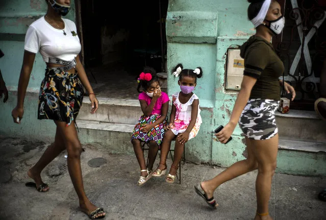 Wearing masks as a precaution against the spread of the new coronavirus Angelica Victoria, center left, and Thalia Oneida, wait for their parents sitting on a chair in Havana, Cuba, Monday, October 12, 2020. Cuba relaxed coronavirus restrictions Monday in hopes of boosting its economy, allowing shops and government offices to reopen and welcoming locals and tourists at airports across the island except in Havana. (Photo by Ramon Espinosa/AP Photo)