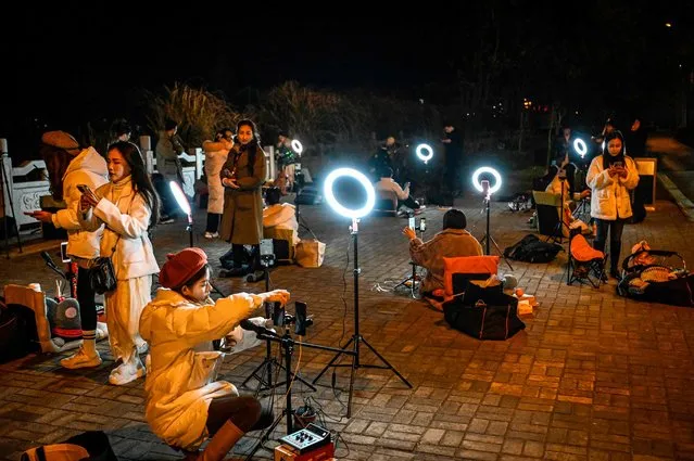 The photo taken on February 20, 2023 shows outdoor livestreamers singing and chatting with the audiences through their mobile phones on an overpass bridge at night in Guilin, in southern China's Guangxi province. In the dead of night on a bridge in southern China, around two dozen livestreamers sat crooning and chatting into microphones, their identical ring lights spaced a few metres apart in glowing rows. (Photo by Jade Gao/AFP Photo)