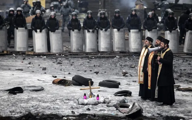 A priest speaks through a megaphone to riot police and anti-government protesters at the site of recent clashes in Kiev, in this February 12, 2014 file photo. (Photo by Konstantin Chernichkin/Reuters)