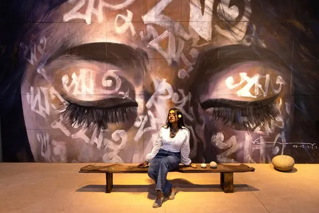 A woman poses in front of an artwork – “Reetu” by artist Bishwajit Goswami, during Dhaka Art Summit at National Art Gallery in Dhaka, Bangladesh on February 12, 2023. Written in Bengali across the face, the word – “Reetu”, meaning “seasons”, is also a commonly used first name for Bengali girls, culturally and symbolically related to the name “Bonna” (Flood) which is the theme of Dhaka Art Summit. Bangladesh is known as “ground zero for climate change” and faces additional stress as nearly 75% of Bangladesh sits below sea level and faces annual floods. Bangladesh has six seasons (and some would argue “had” as climate change has made two seasons difficult to recognize anymore) each harkening to a particular mood, feelings, and cultural practices. Human life can also be measured in seasons. Goswami connects these personal stories of land, nature, and seasons with words, pigment, and touch. Fragments of memory enable a sensorial, intimate exchange of feelings and words to take place with the artist, and within the self, manifesting in moving drawings connecting our inner and outer worlds. (Photo by Joy Saha/Rex Features/Shutterstock)
