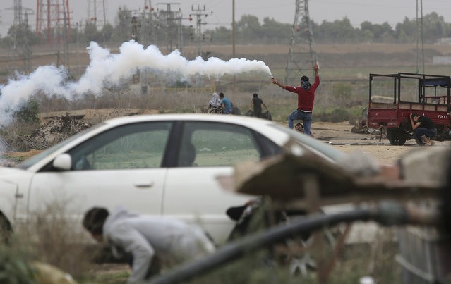 A Palestinian protester holds a tear gas canister as others cover themselves during clashes with Israeli soldiers on the Israeli border Eastern Gaza City, Friday, November 6, 2015. (Photo by Adel Hana/AP Photo)