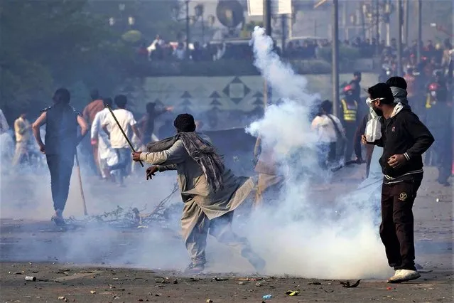 A supporter of former Prime Minister Imran Khan hurls back a tear gas shell fired by riot police officers to disperse them during clashes, in Lahore, Pakistan, Wednesday, March 15, 2023. Clashes between Pakistan's police and supporters of Khan continued outside his home in the eastern city of Lahore on Wednesday, a day after officers went to arrest him for failing to appear in court on graft charges. (Photo by K.M. Chaudary/AP Photo)
