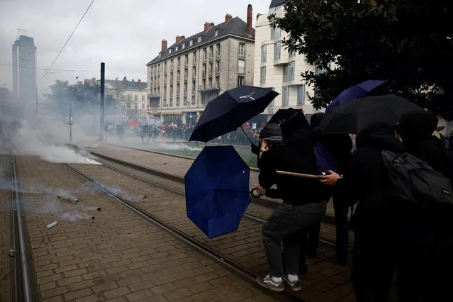 Protesters protect themselves with umbrellas amid tear gas during clashes at a demonstration as part of the ninth day of nationwide strikes and protests against French government's pension reform, in Nantes, France on March 23, 2023. (Photo by Stephane Mahe/Reuters)