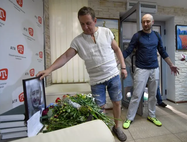 Anti-Kremlin journalist Arkady Babchenko reacts as he arrives in the offices of his workplace, the ATR TV channel, where his colleagues laid flowers by a portrait of him in his memory, on May 31, 2018 in Kiev a day following his shock reappearance after Ukrainian authorities said he had been shot dead. In an operation that blindsided the world's media, Babchenko made a shock reappearance at a press conference in Kiev on May 31, less than 24 hours after the Ukrainian authorities reported he had been shot dead at his home in a contract-style killing blamed on Russia. (Photo by Genya Savilov/AFP Photo)
