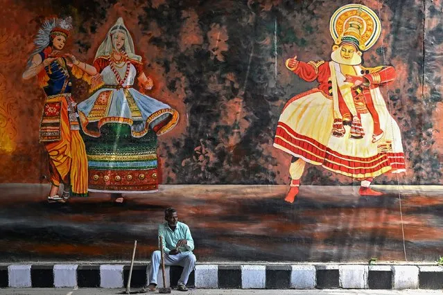 A labourer sits in front of a mural depicting Indian traditional dance forms Kathakali (R) and Manipuri painted under a bridge in New Delhi on June 22, 2023. (Photo by Arun Sankar/AFP Photo)