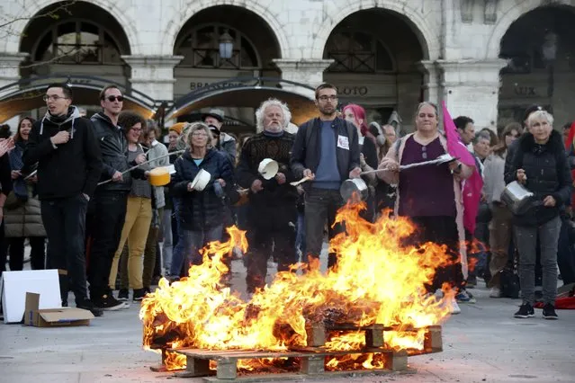 People bang pots and pans behind burning palettes while French President Emmanuel Macron seeks to diffuse tensions in a televised address to the nation, Monday, April 17, 2023 in Bayonne, southwestern France. Emmanuel Macron said Monday that he heard people's anger over raising the retirement age from 62 to 64, but insisted that it was needed. (Photo by Bob Edme/AP Photo)