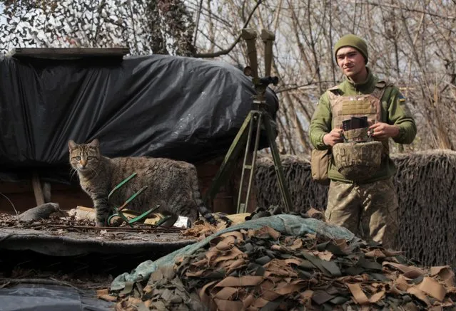 A cat walks as a service member of the Ukrainian armed forces stands guard at fighting positions on the line of separation near the rebel-controlled city of Donetsk, Ukraine on April 16, 2021. (Photo by Serhiy Takhmazov/Reuters)
