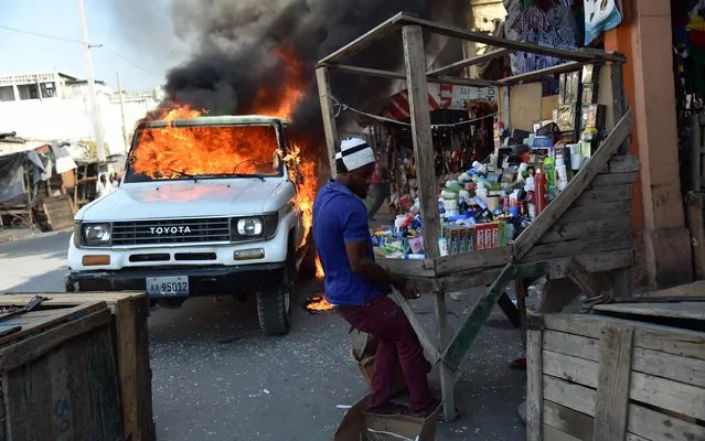 Traders try to rescue their merchandise near a burning car during a protest in Port-au-Prince, on January 18, 2016. During the protest the demonstrators blocked some street with burning tires and two cars were burned. The second round of presidential elections is scheduled on January 24, between ruling party candidate Jovenel Moise and Jude Celestin. Celestin has said he is not participating in the January 24 elections but has not yet presented his offitial resignation to the Provisional Electoral Council (CEP). (Photo by Hector Retamal/AFP Photo)