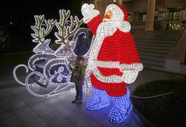 A child poses for pictures in front of Christmas decorations in Mytilene, in the northeastern island of Lesbos, Greece, Thursday, December 15, 2016. Photo by Lefteris Pitarakis/(AP Photo)