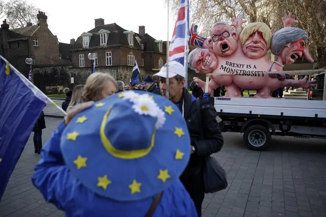 A remain in the European Union, anti-brexit sculpture is displayed as a protester wearing a European flag design hat stands demonstrating in the foreground across the street from the House of Parliament in London, Tuesday, December 11, 2018. Top European Union officials are ruling out any renegotiation of the divorce agreement with Britain as Prime Minister Theresa May fights to save her Brexit deal by lobbying leaders in Europe's capitals. (Photo by Matt Dunham/AP Photo)