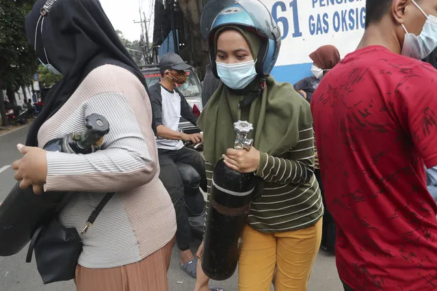 A woman carries her oxygen tank after having it refilled at a recharging station in Jakarta, Indonesia, Friday, July 9, 2021. The world's fourth most populous country is running out of oxygen as it endures a devastating wave of coronavirus cases and the government is seeking emergency supplies from other countries, including Singapore and China. (Photo by Tatan Syuflana/AP Photo)