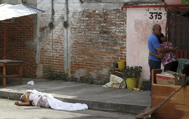 In this Wednesday, January 2, 2019 photo, a man's body lies on the pavement after he was shot to death, as his parents hug nearby in Acapulco, Mexico. (Photo by Bernardindo Hernandez/AP Photo)